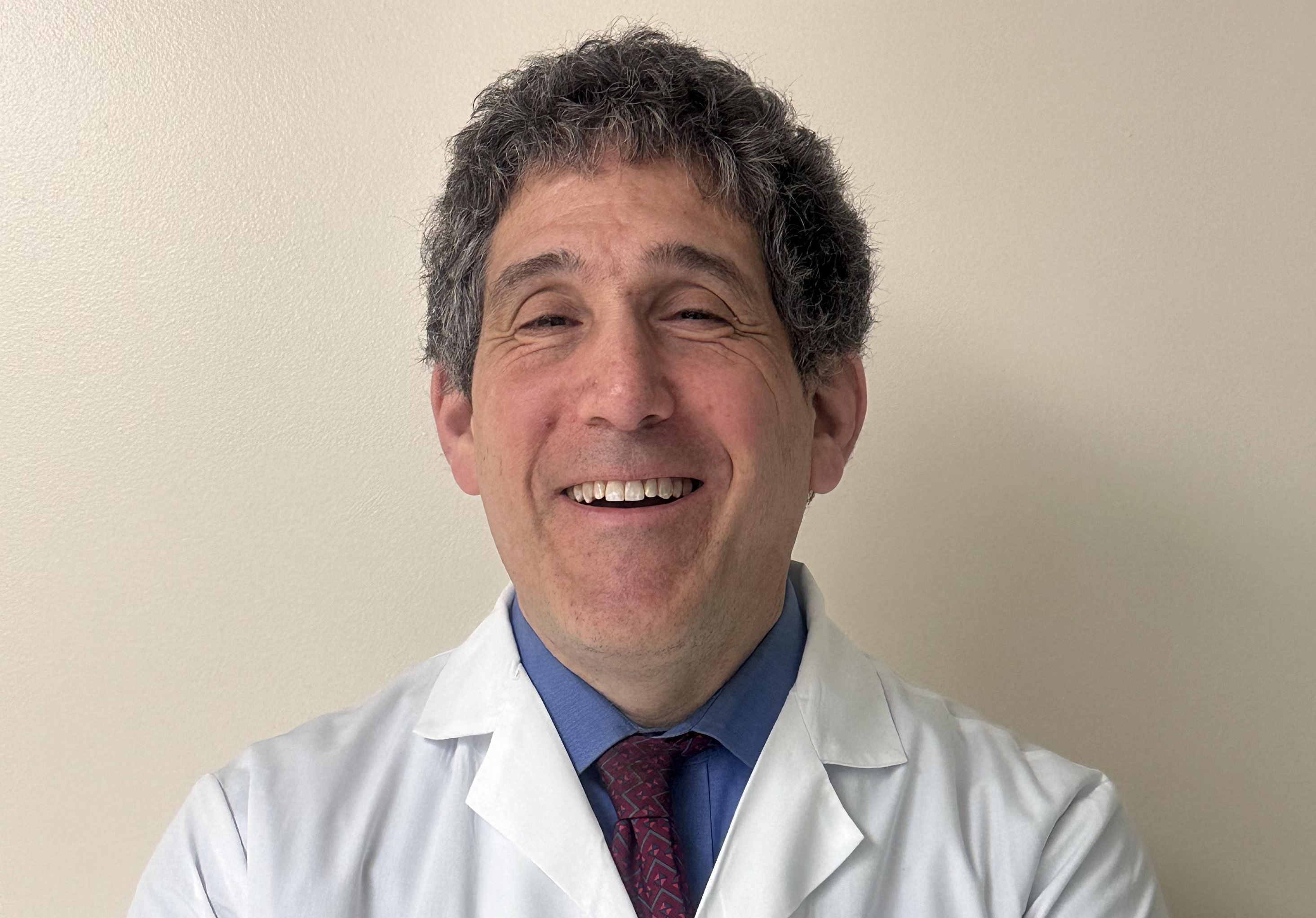 Eric Altschuler, M.D., in a white coat and dress shirt smiling