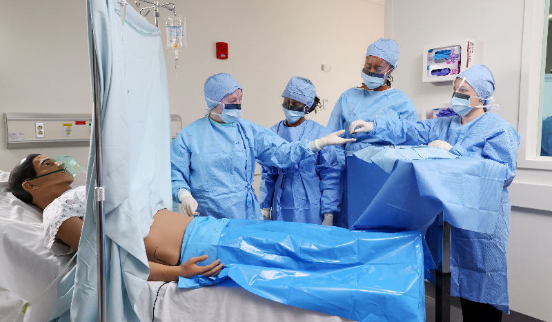 Students in blue scrubs gathered around manikin
