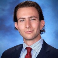 man with dark hair wearing dark suit and red tie