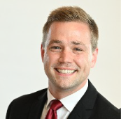 man with blond hair wearing dark suit and red tie