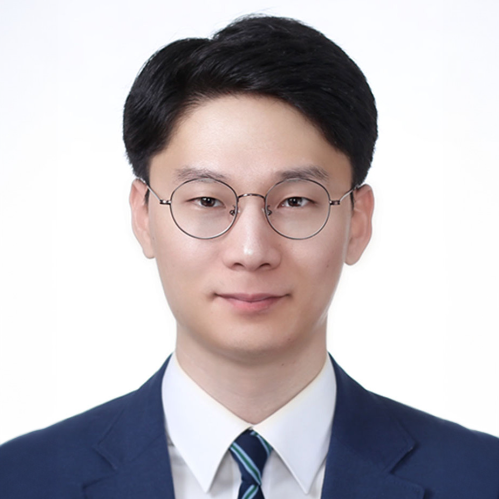 dark haired man wearing glasses and blue suit and tie in front of white background