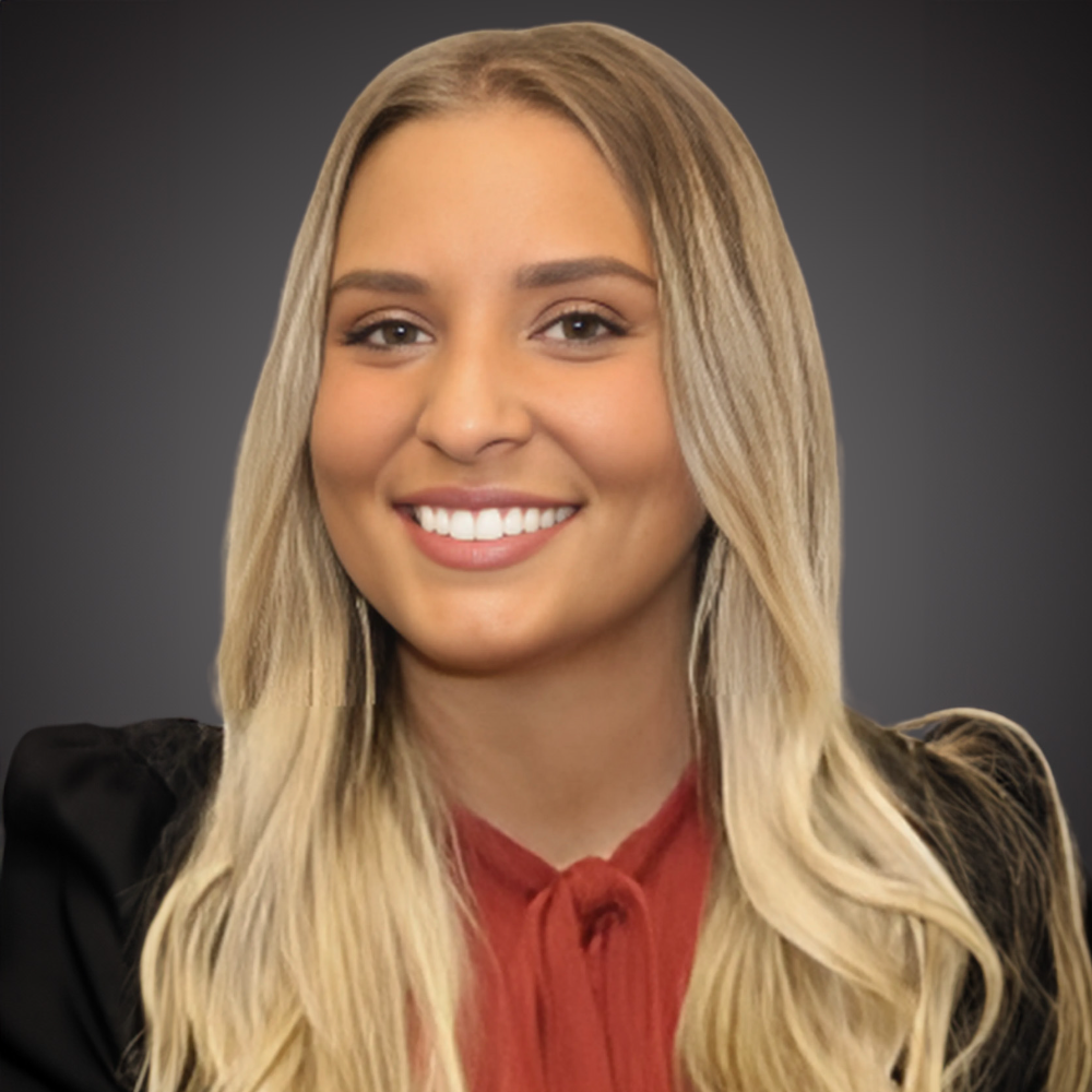 blond woman wearing red top and black jacket with gray background
