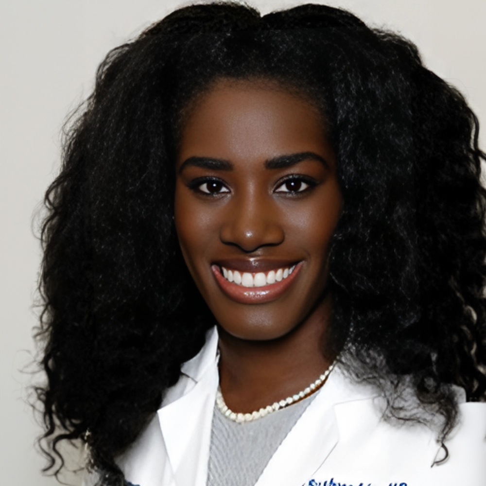 Black woman with long hair wearing white coat in front of light gray background