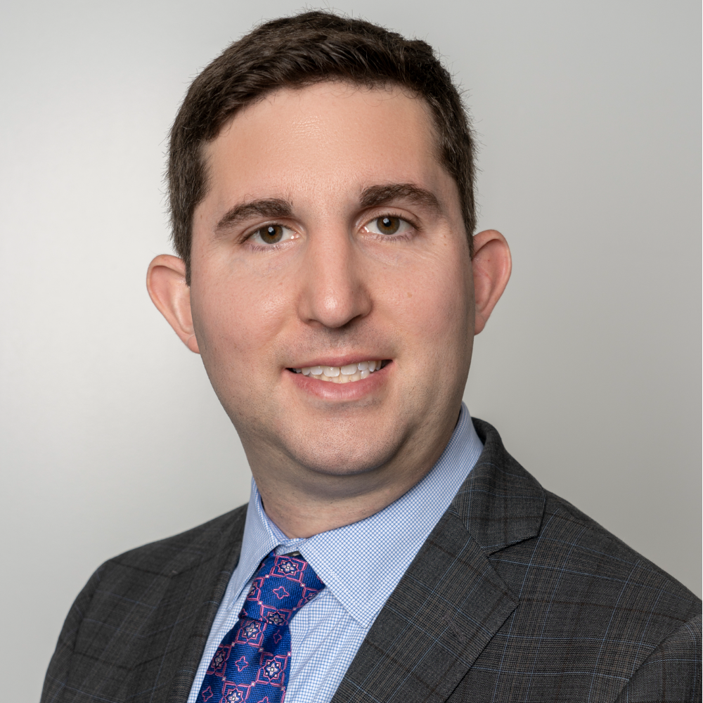 man with short dark hair wearing gray suit with blue shirt and tie