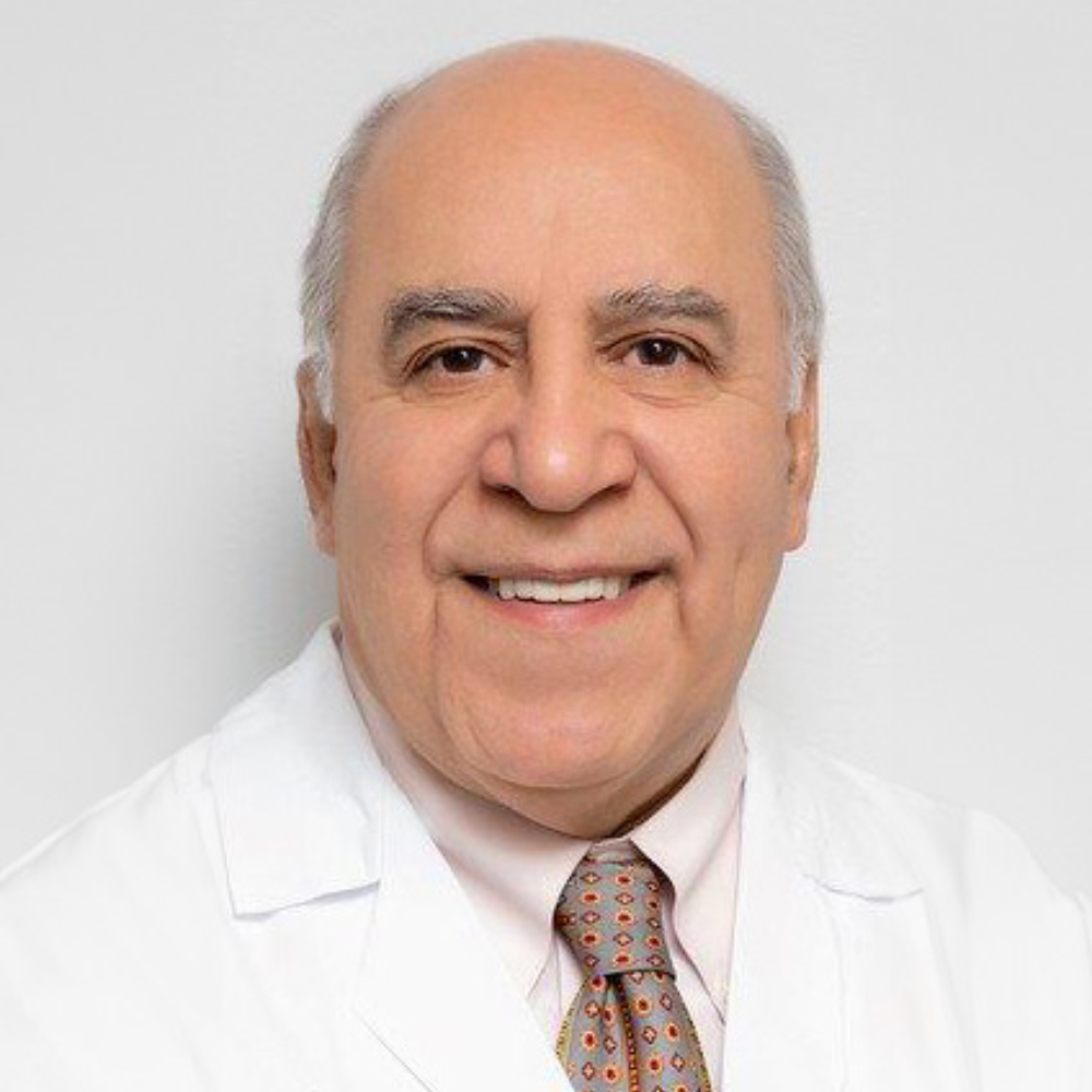 balding man wearing white coat and tie in front of light gray background
