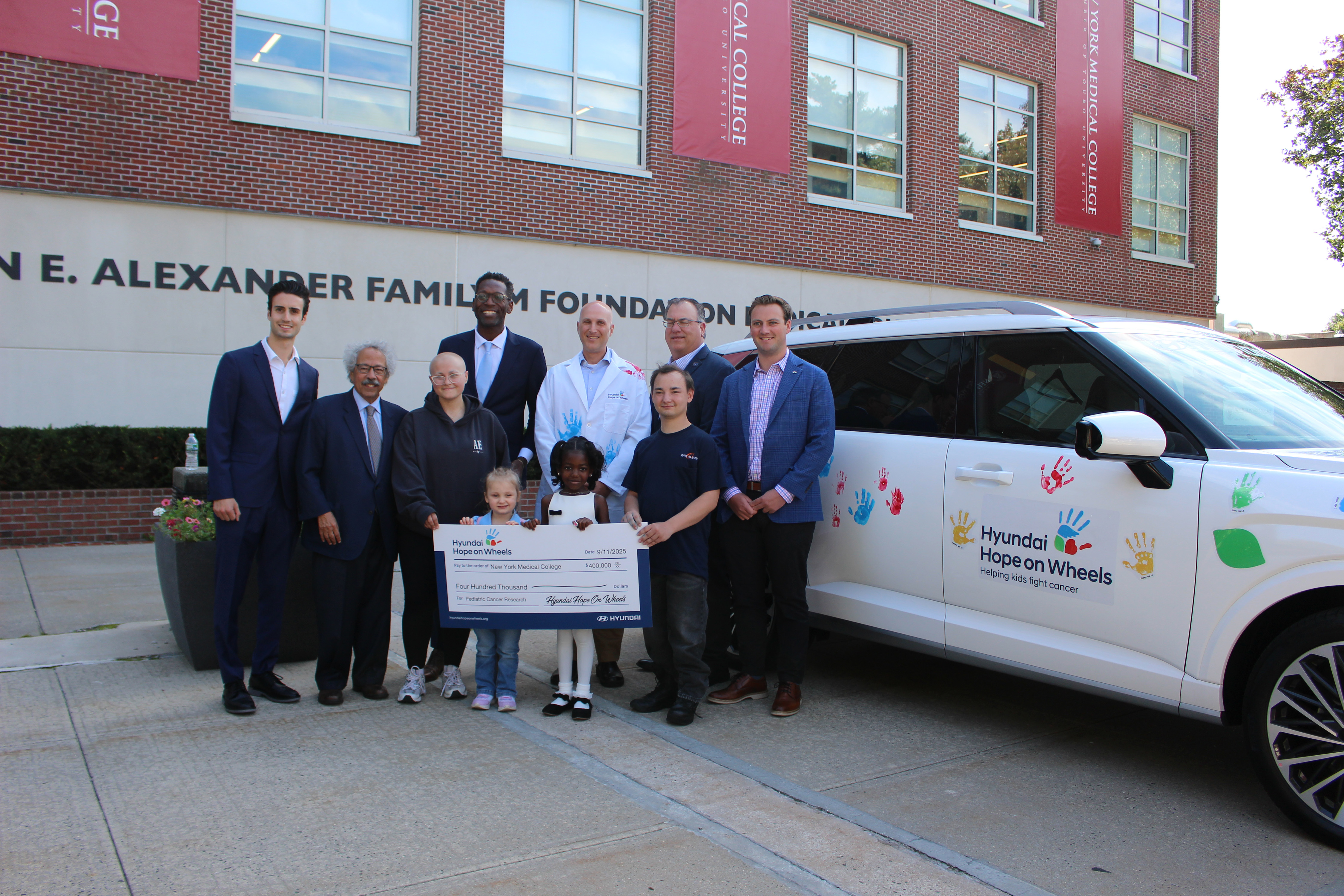 Adults and children holding a big check next to a vehicle with handprints.