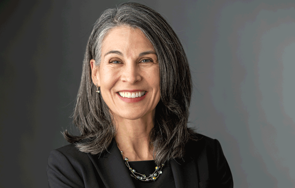 Dr. Ludmer wearing a black dress shirt and suit jacket smiling in front of a gray background.