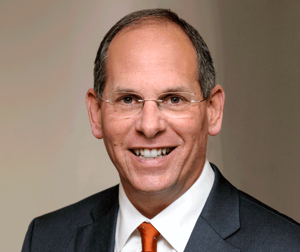 Dr. Schluger wearing glasses, a white collar shirt and suit jacket staring forward.