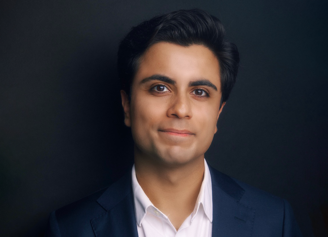 A man with a dress shirt and suit jacket smiling.