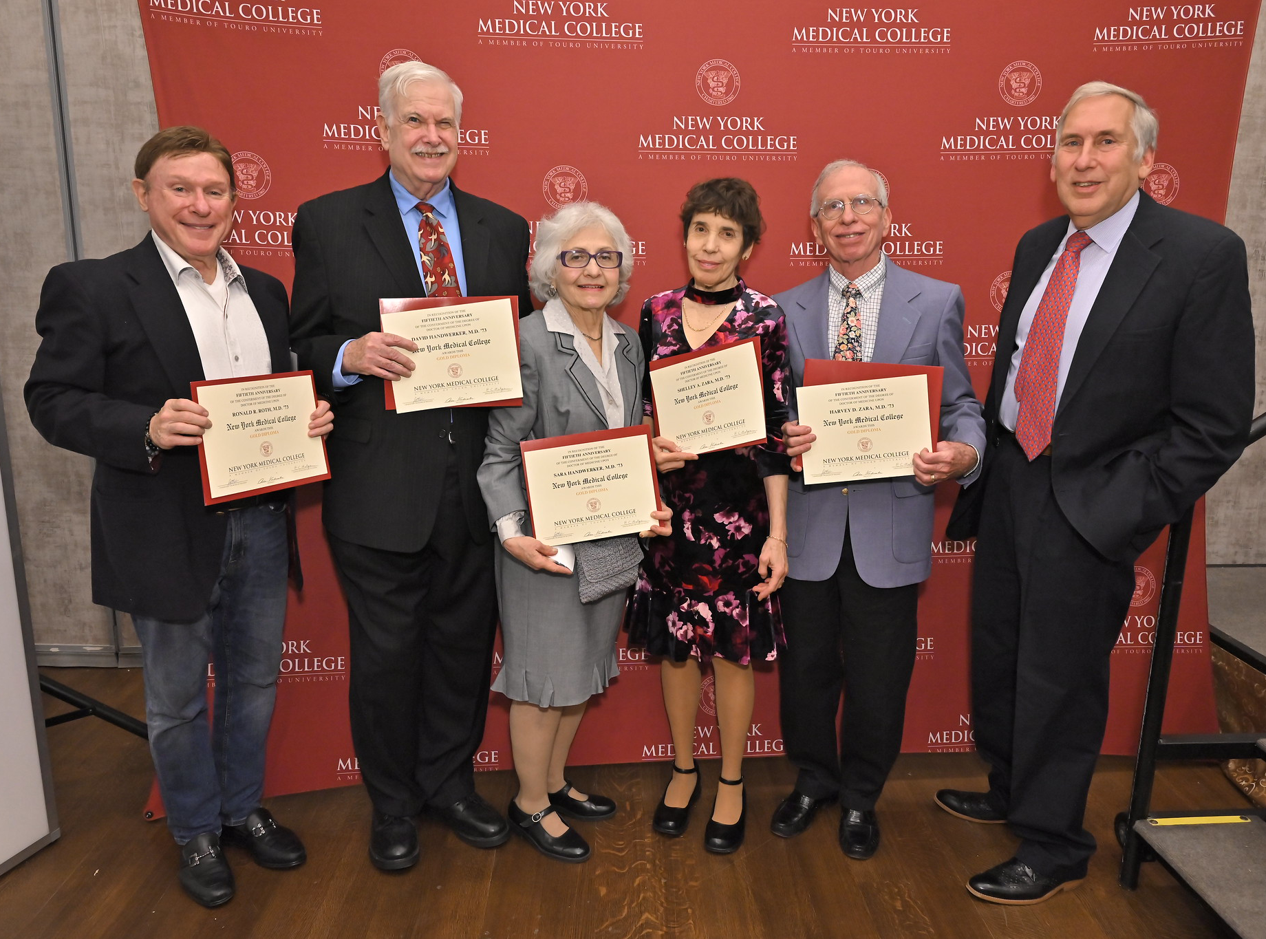 Men and women accepting awards smiling in front of New York Medical College backdrop.