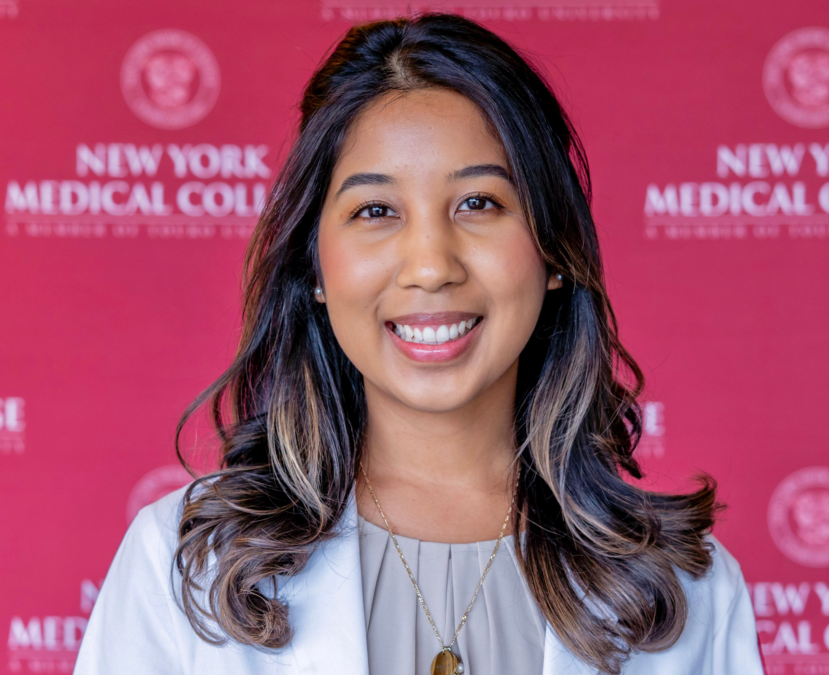 Woman with long hair in a white coat smiling in front of a step and repeat