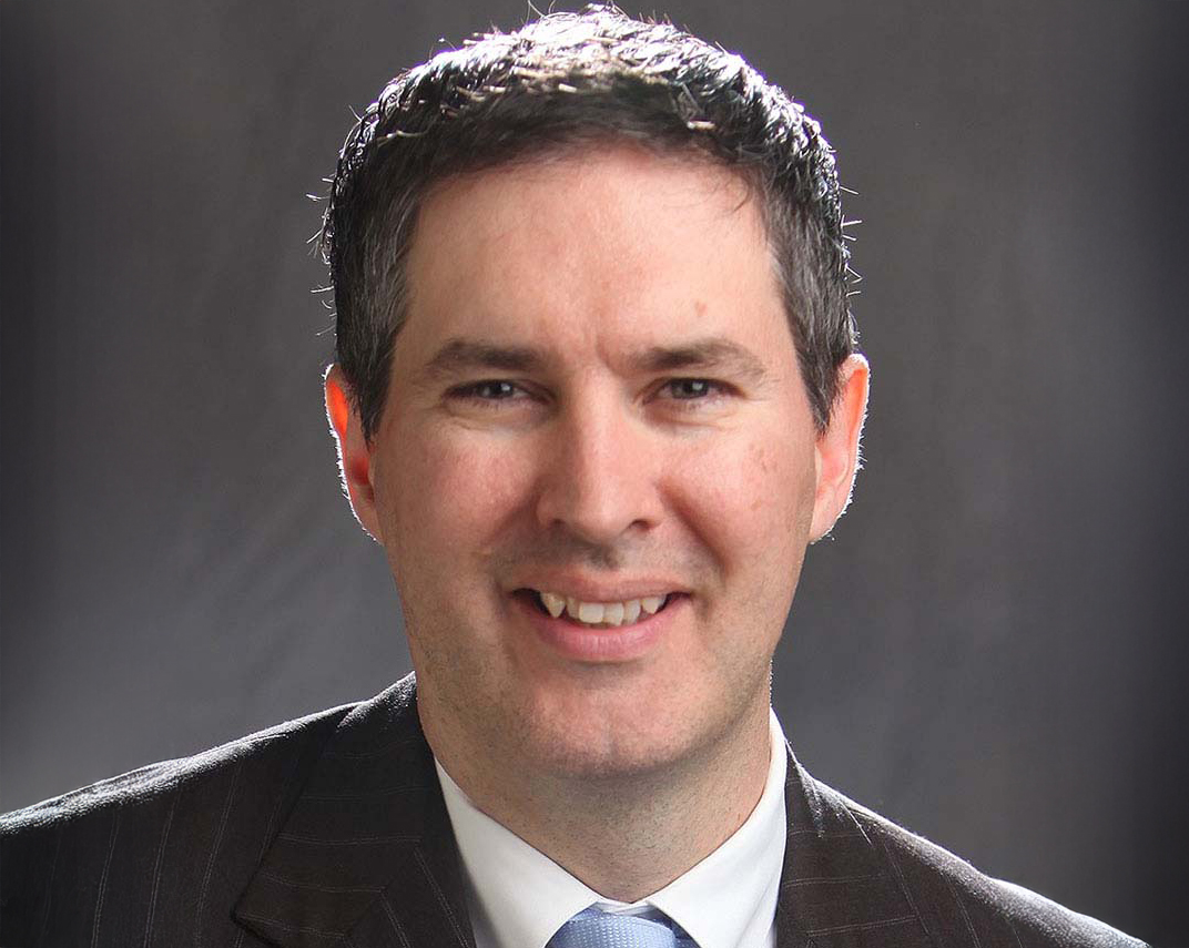 Man wearing suit and tie smiling in front of dark backdrop