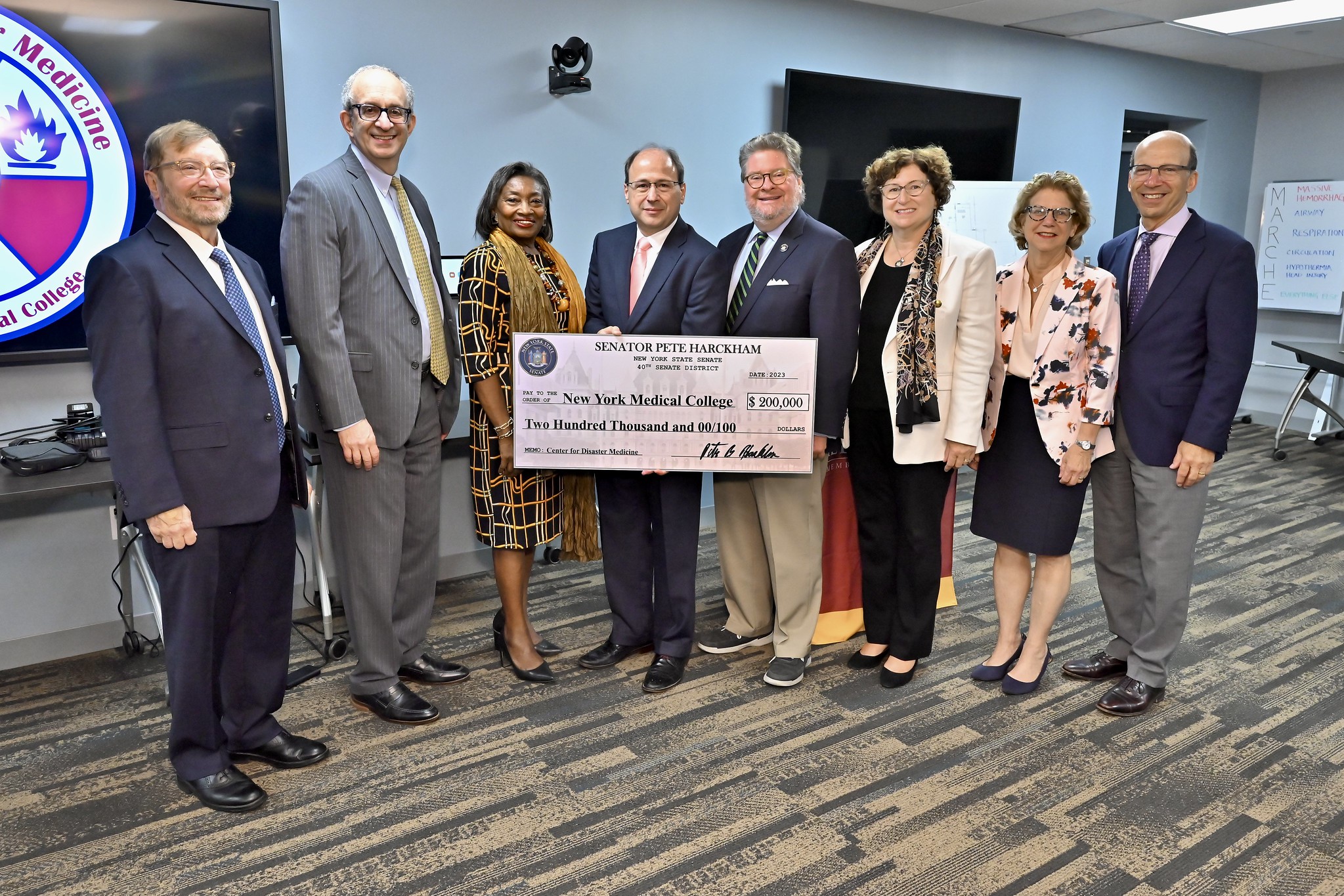 A diverse group of men and women in suits and dresses smiling as they hold a giant check.