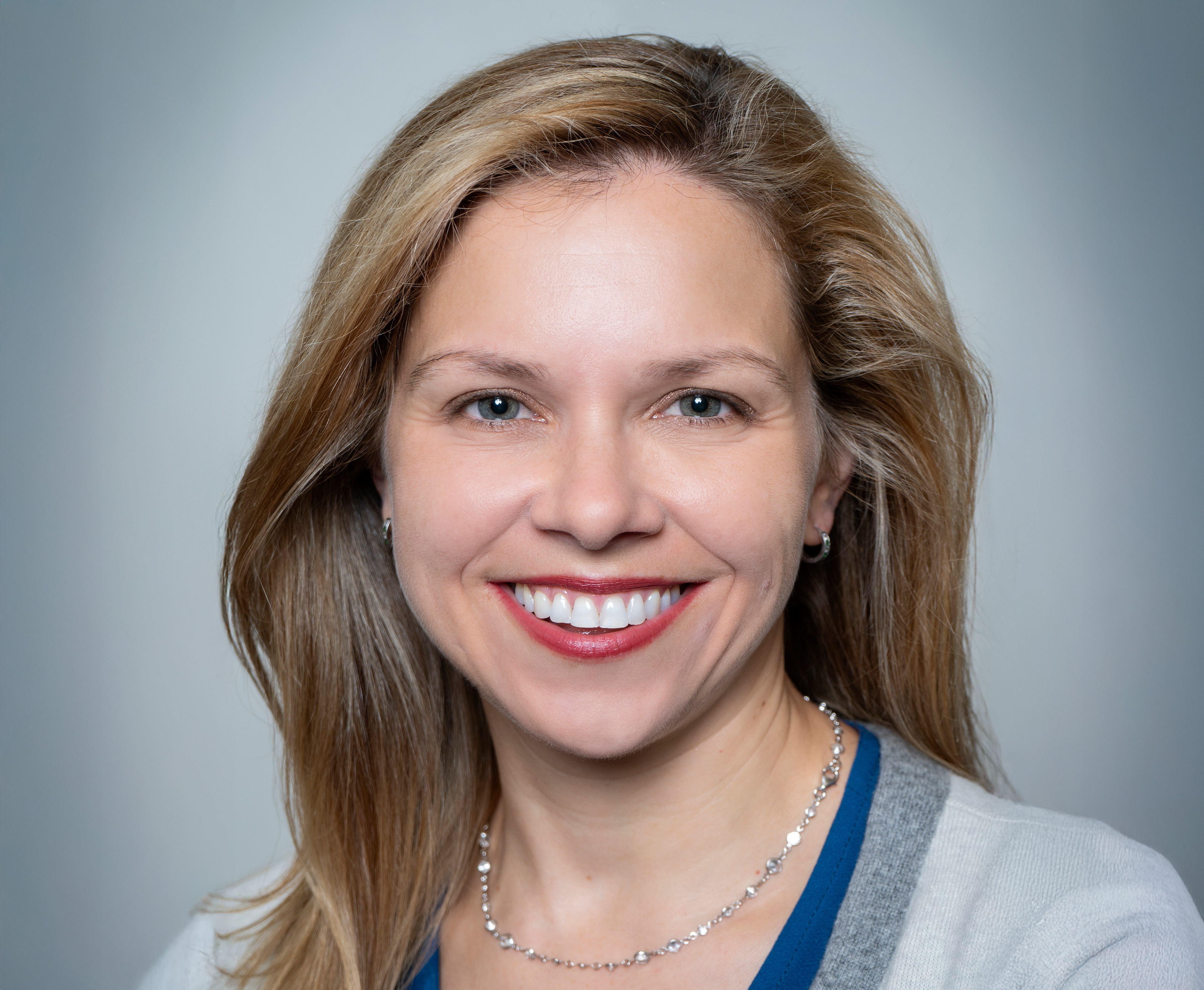 Woman wearing a sweater smiling in front of plain background.
