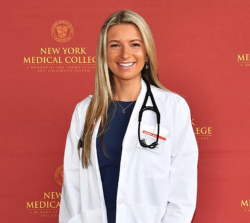 Woman with blond hair wearing a white lab coat smiling in front of NYMC backdrop
