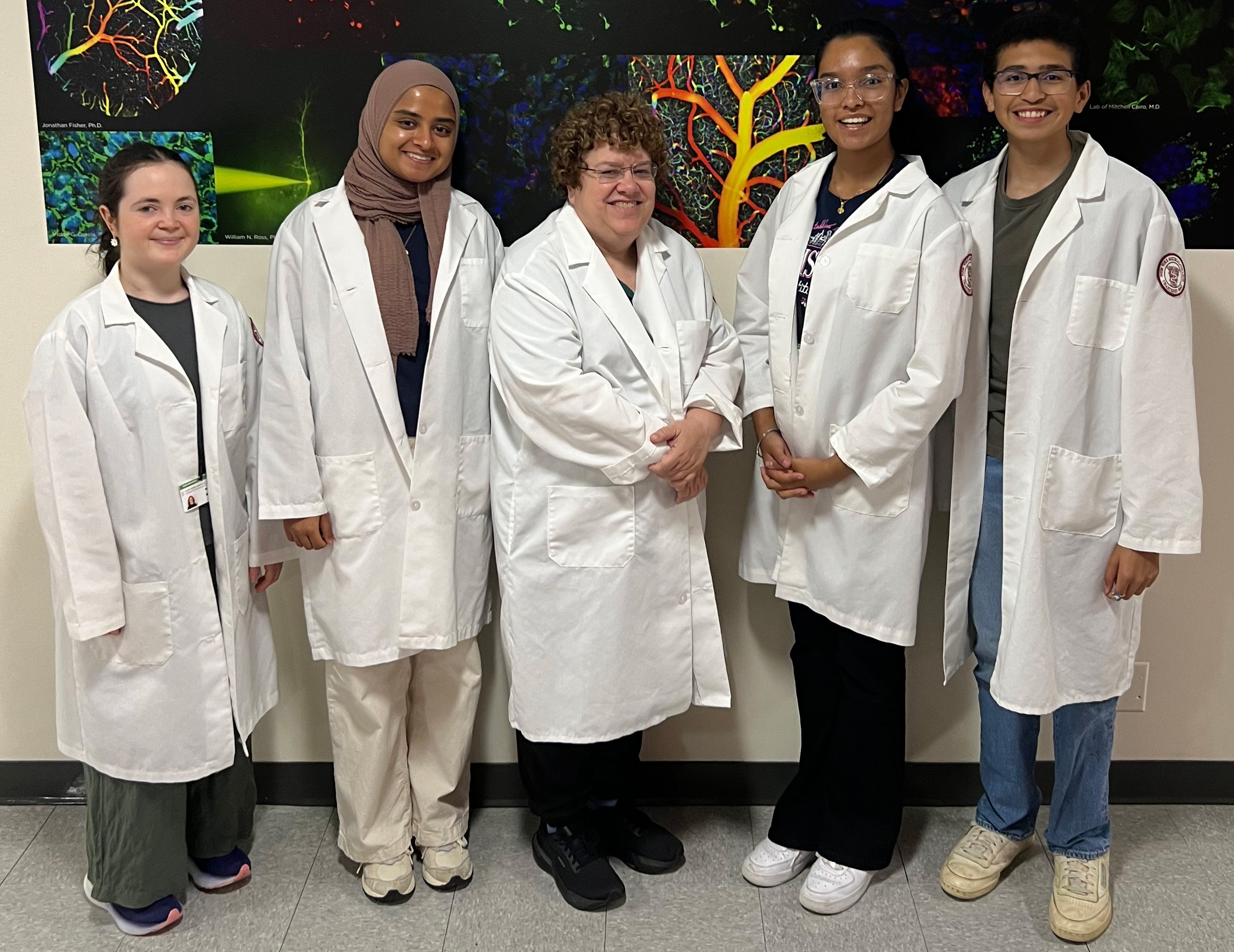 Men and women wearing white lab coats in front of research photos