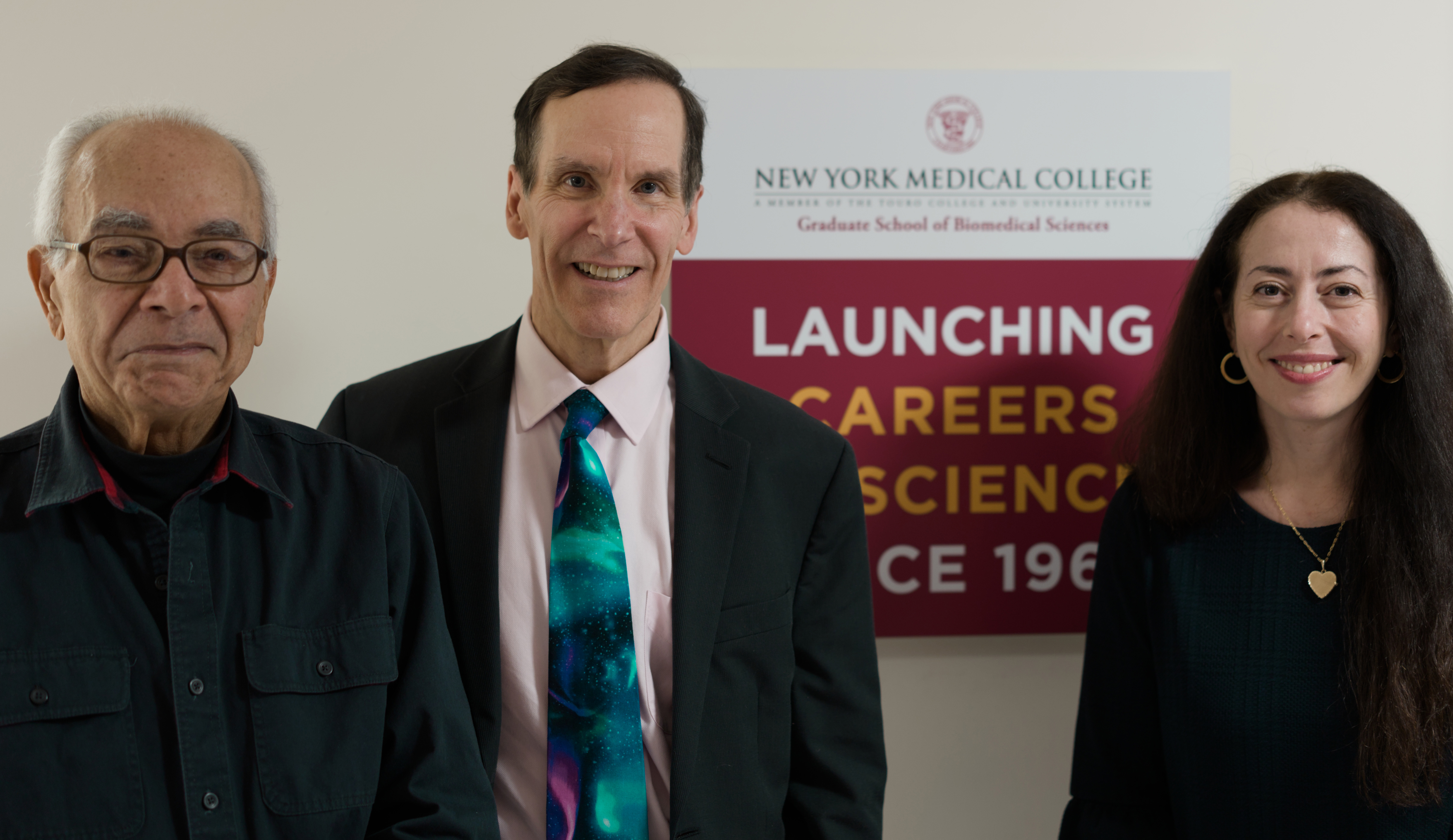 Two men and a woman in formal dress ware in smiling indoors
