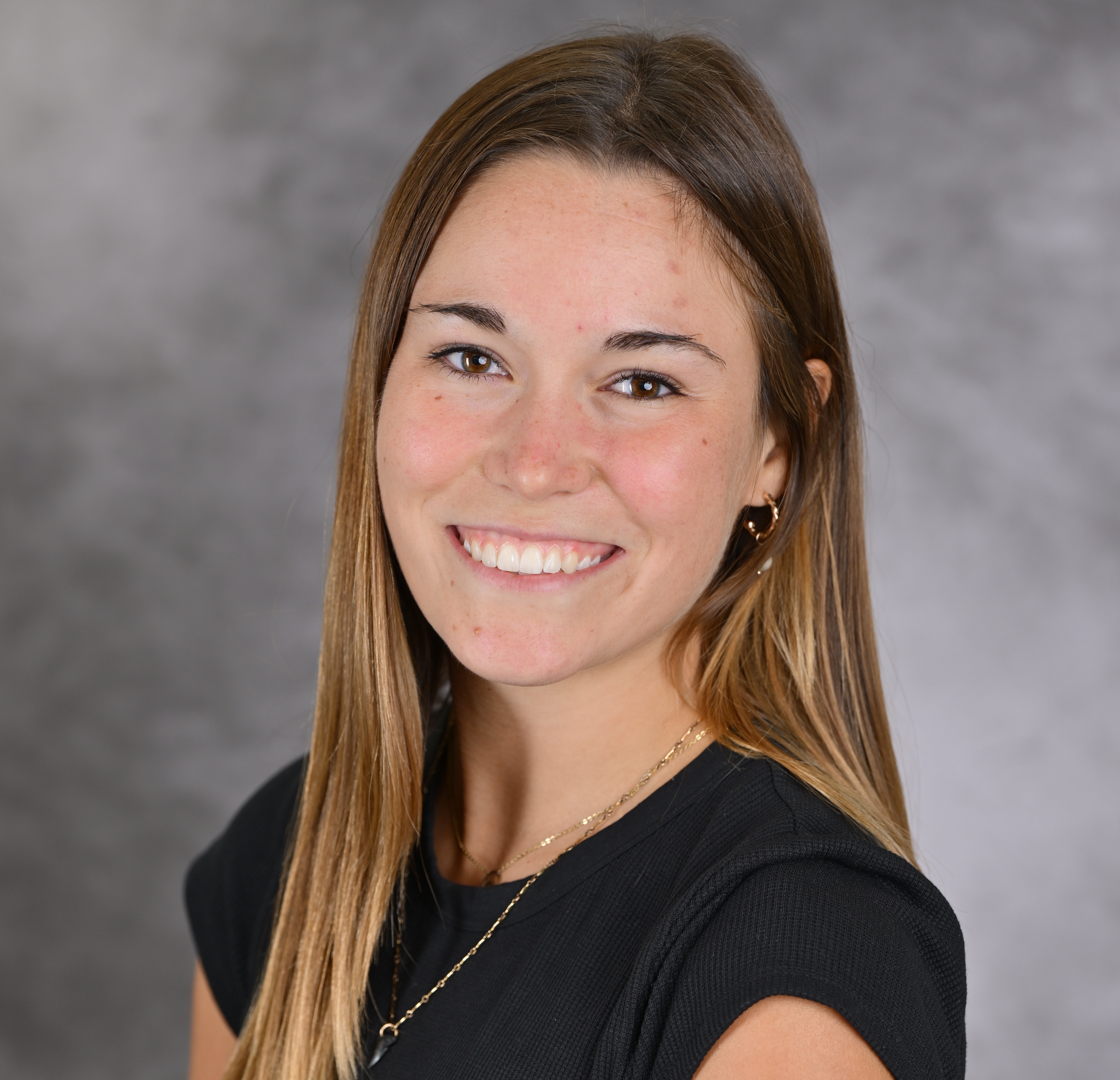 Girl smiling in front of grey background wearing black shirt