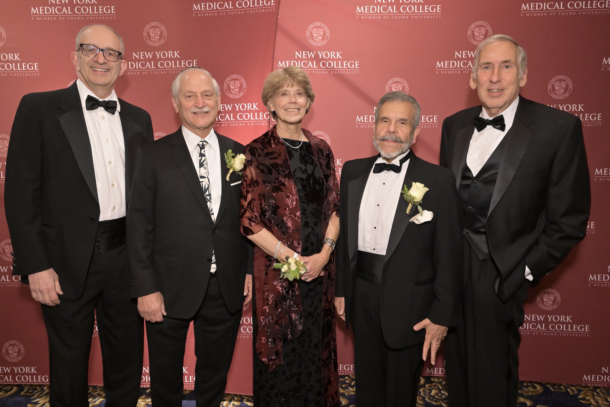 Four men and a woman dressed in formal clothing smiling in front of a step and repeat.