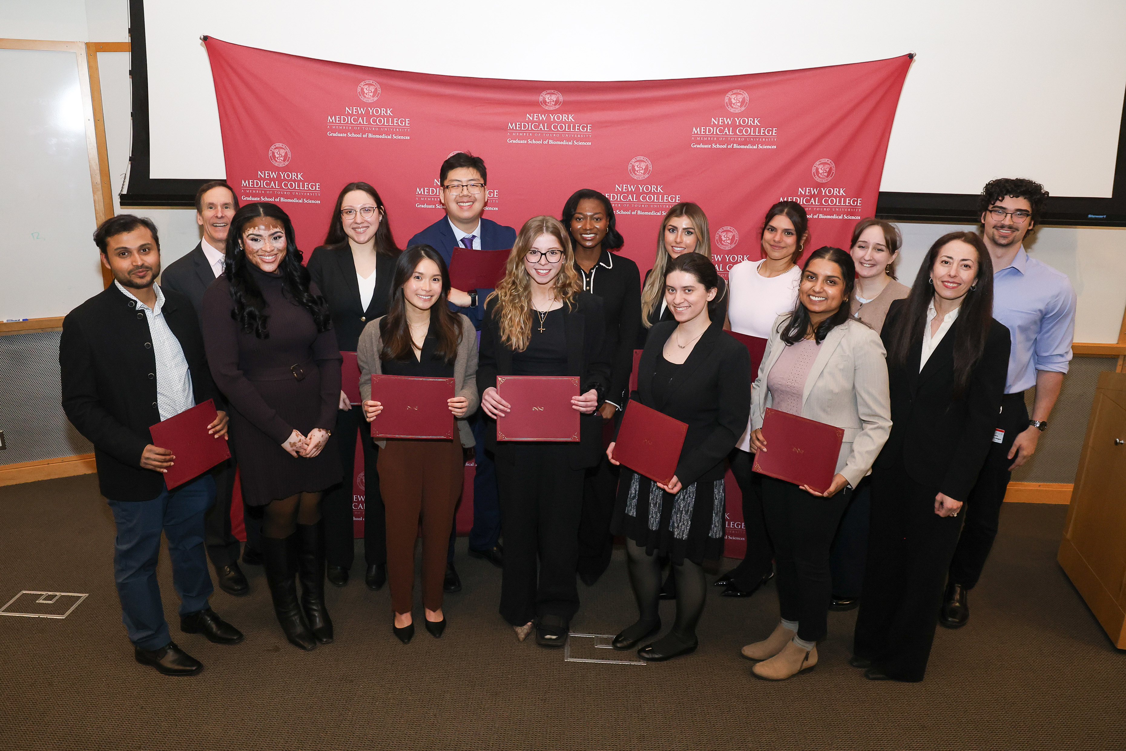 Students in business formal attire in front of step and repeat with award folders in hand.