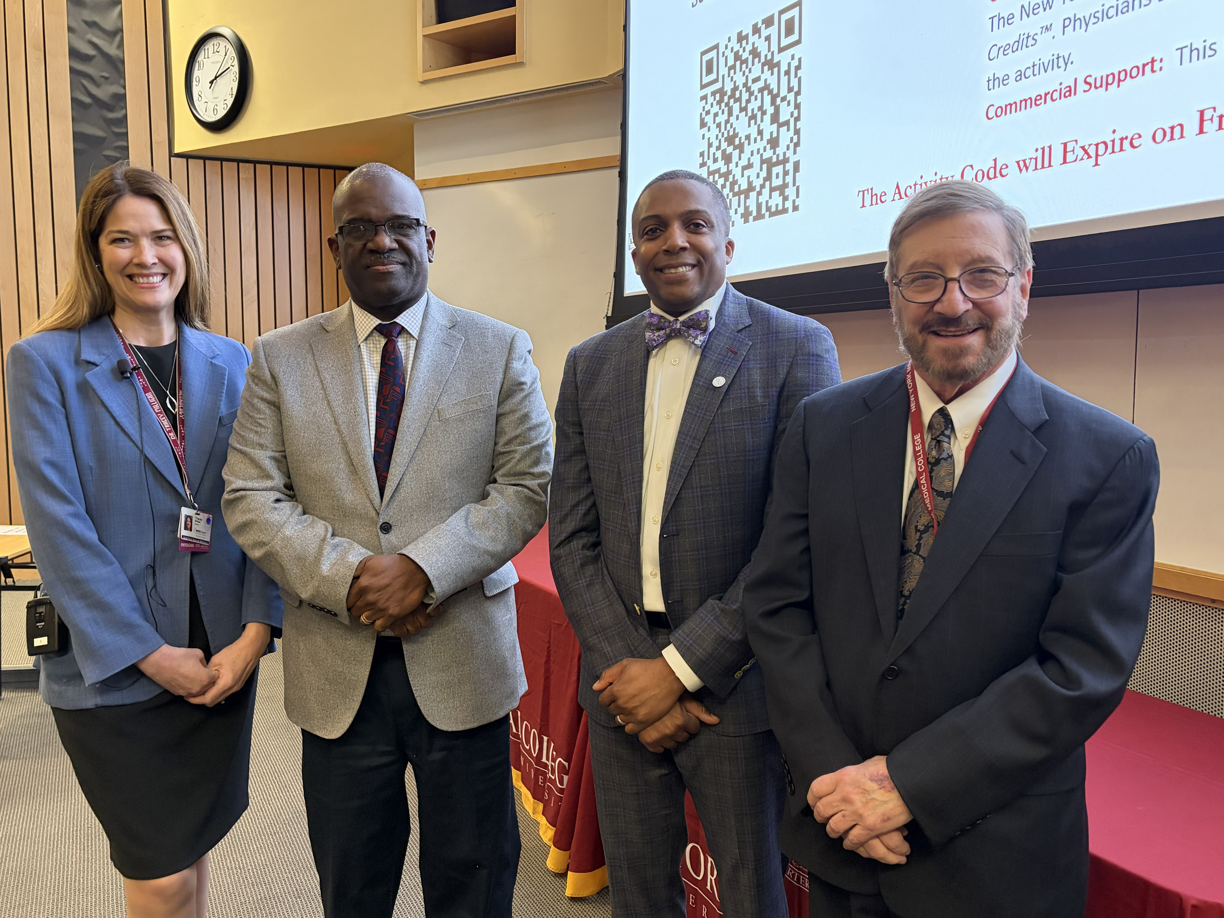 A woman and three men in an auditorium smiling in formal attire