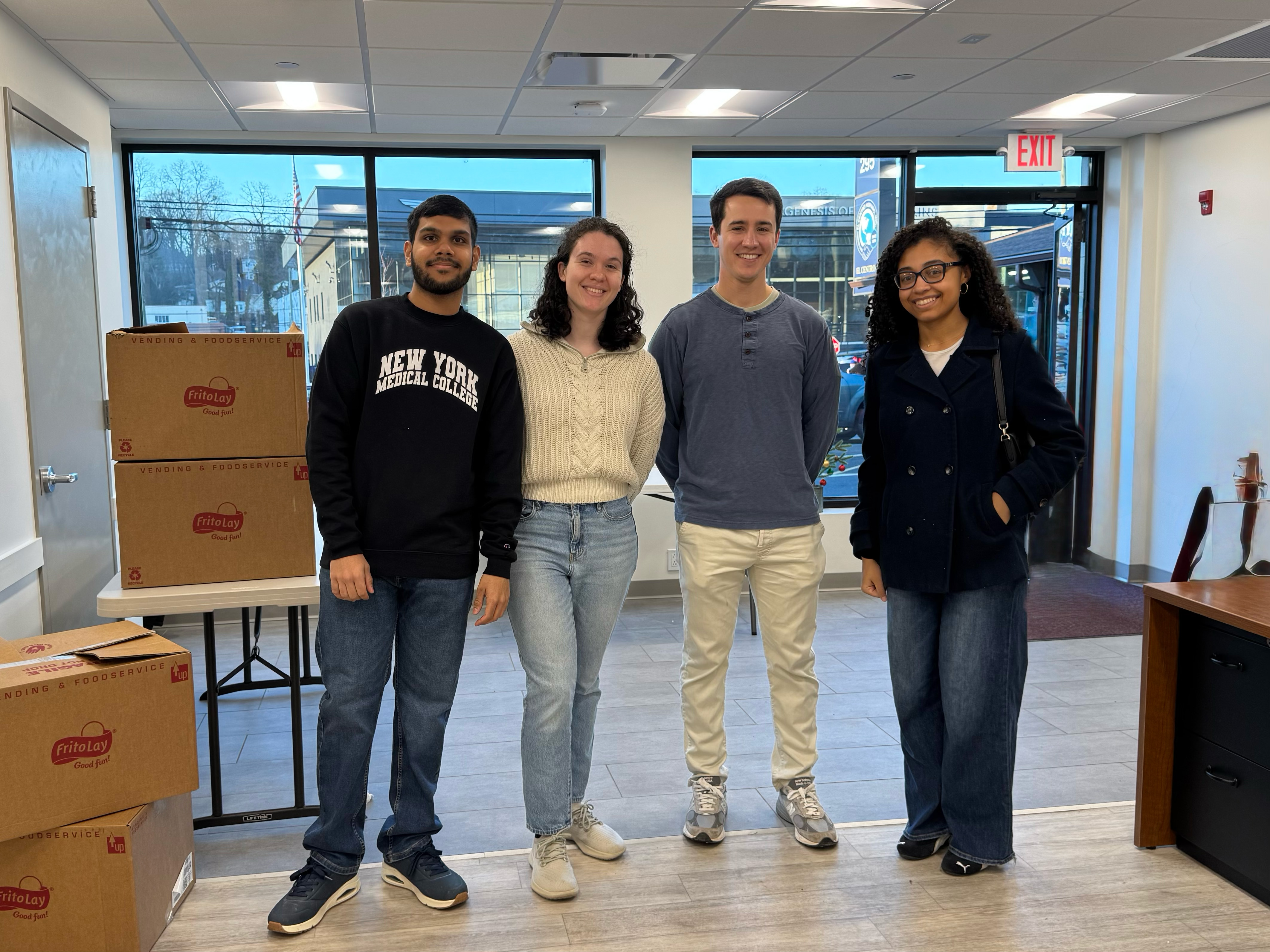 4 diverse male and female students standing by food distribution boxes indoors