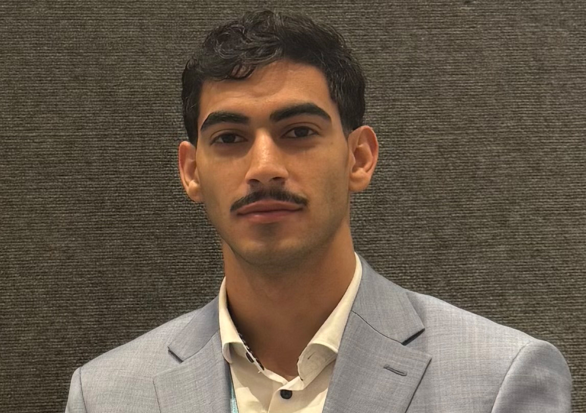 A young man wearing a dress shirt and blazer smiling 