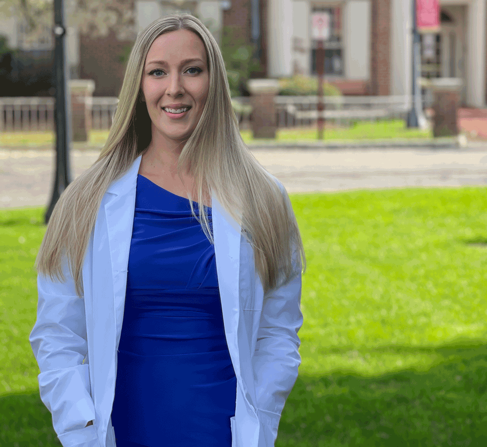Jena Schoenherr, Doctor of Physical Therapy Class of 2023 in a blue dress and white coat outside in front of the Sunshine Building