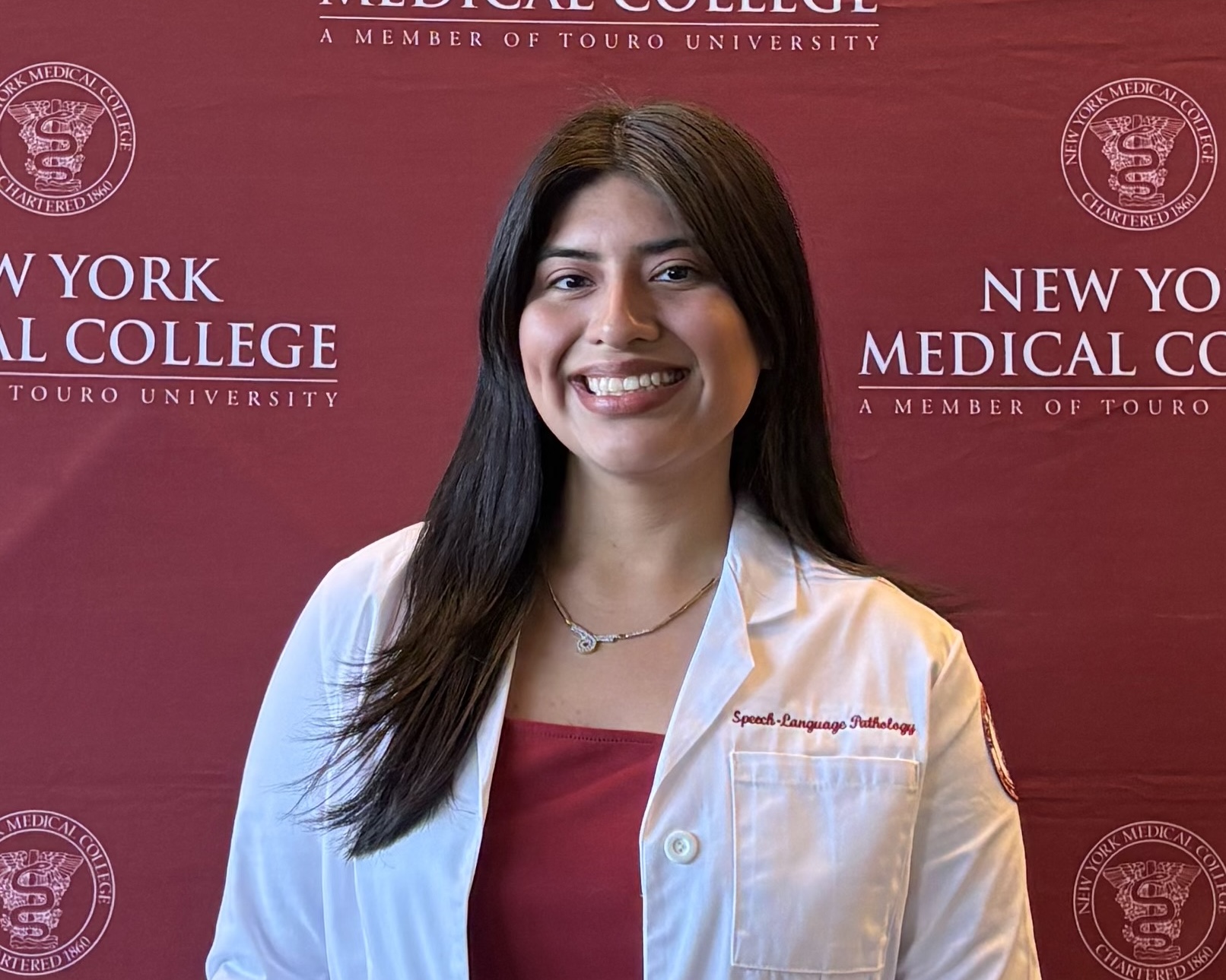 Student smiling in white coat in front of maroon background