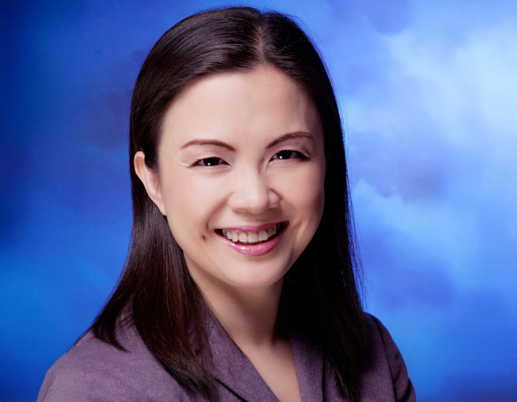 Asian woman with dark hair and mauve shirt smiling in front of sky background