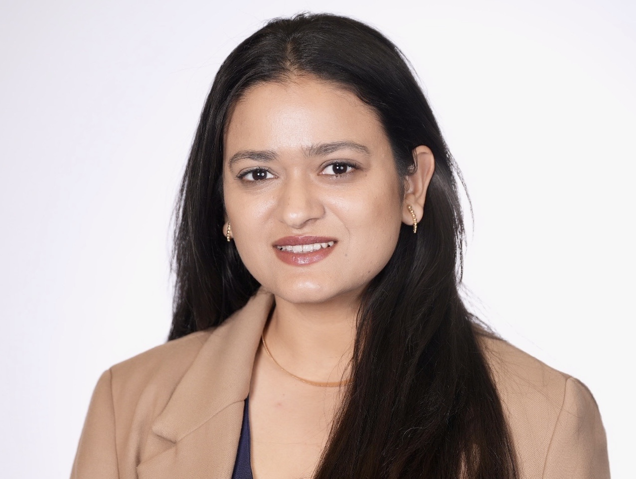 Woman smiling with dark hair wearing a light brown blazer in front of a white backdrop