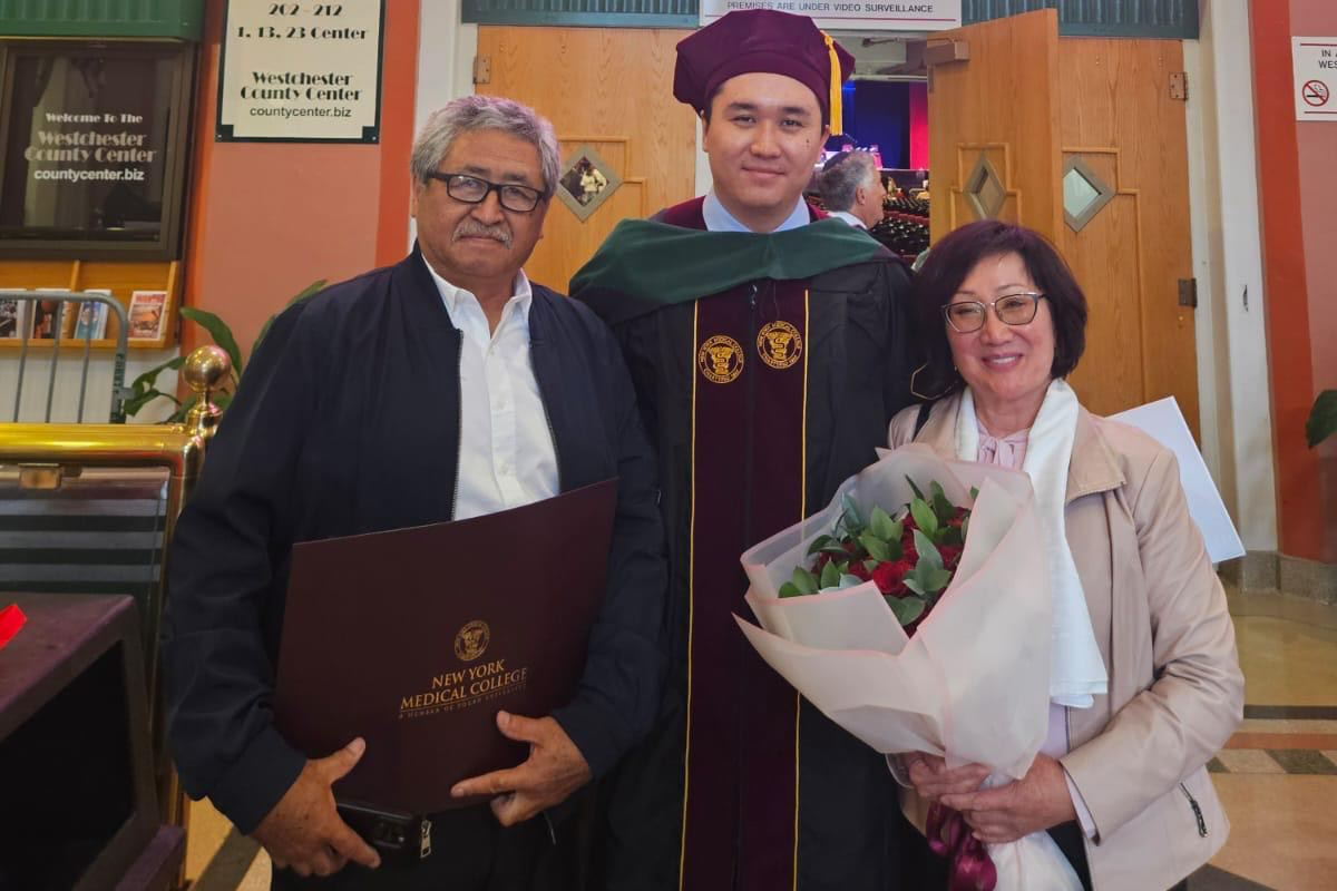 Medical student graduate in academic attire with parents holding diploma and flowers