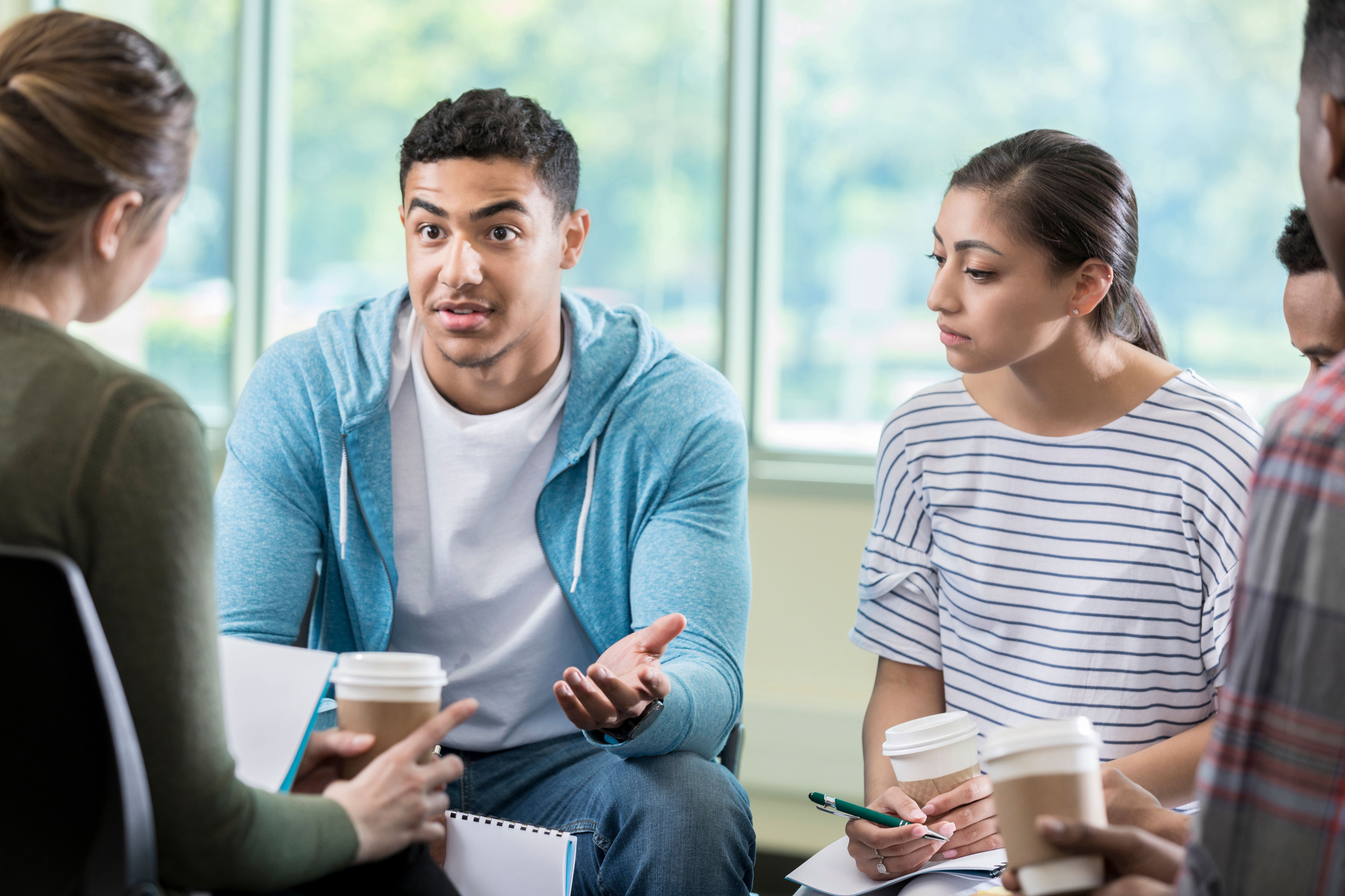 A man and woman in a group speaking with notebooks and coffee