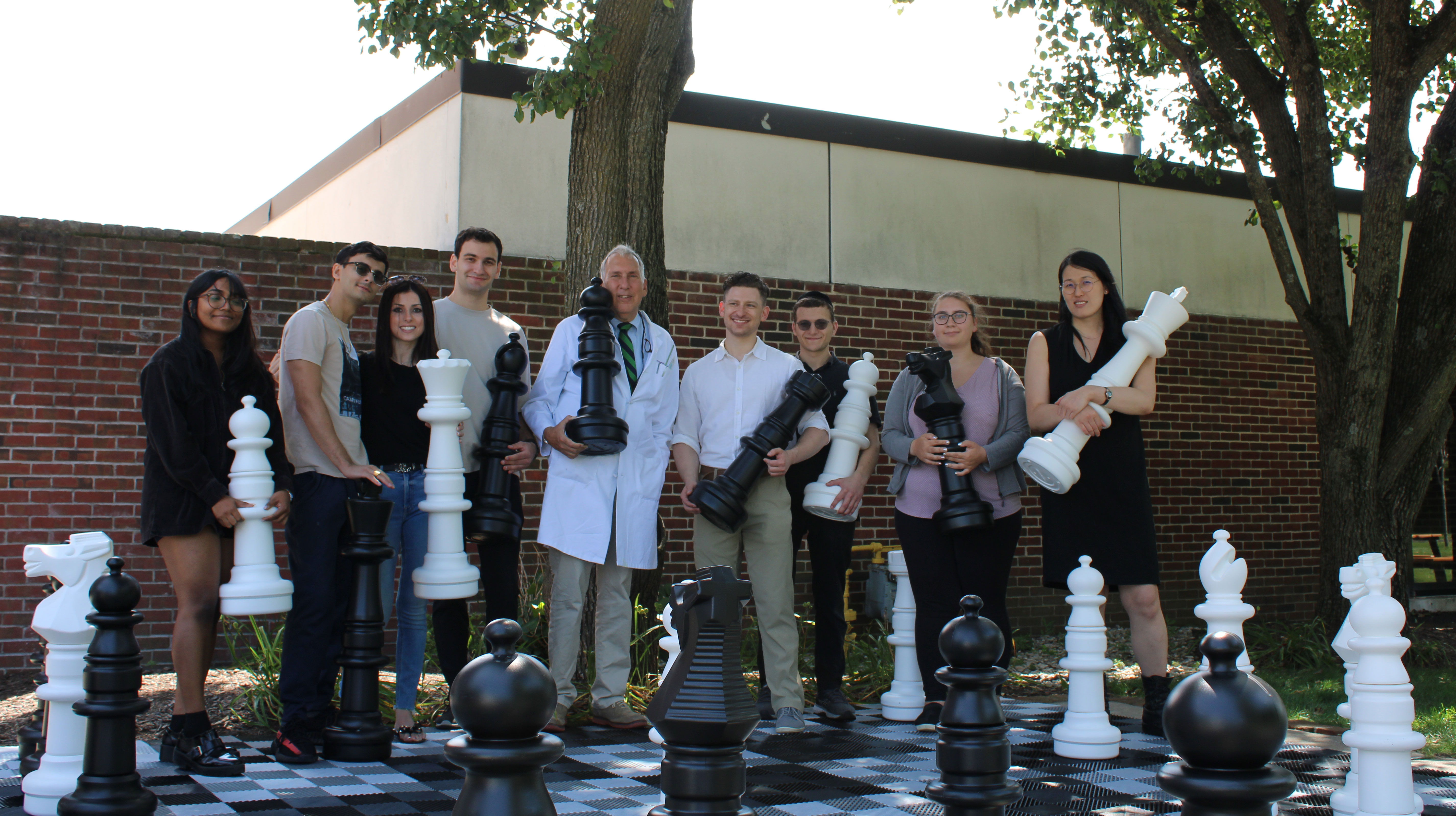 Students and leadership holding jumbo chess pieces in front of a jumbo chess board on the floor.
