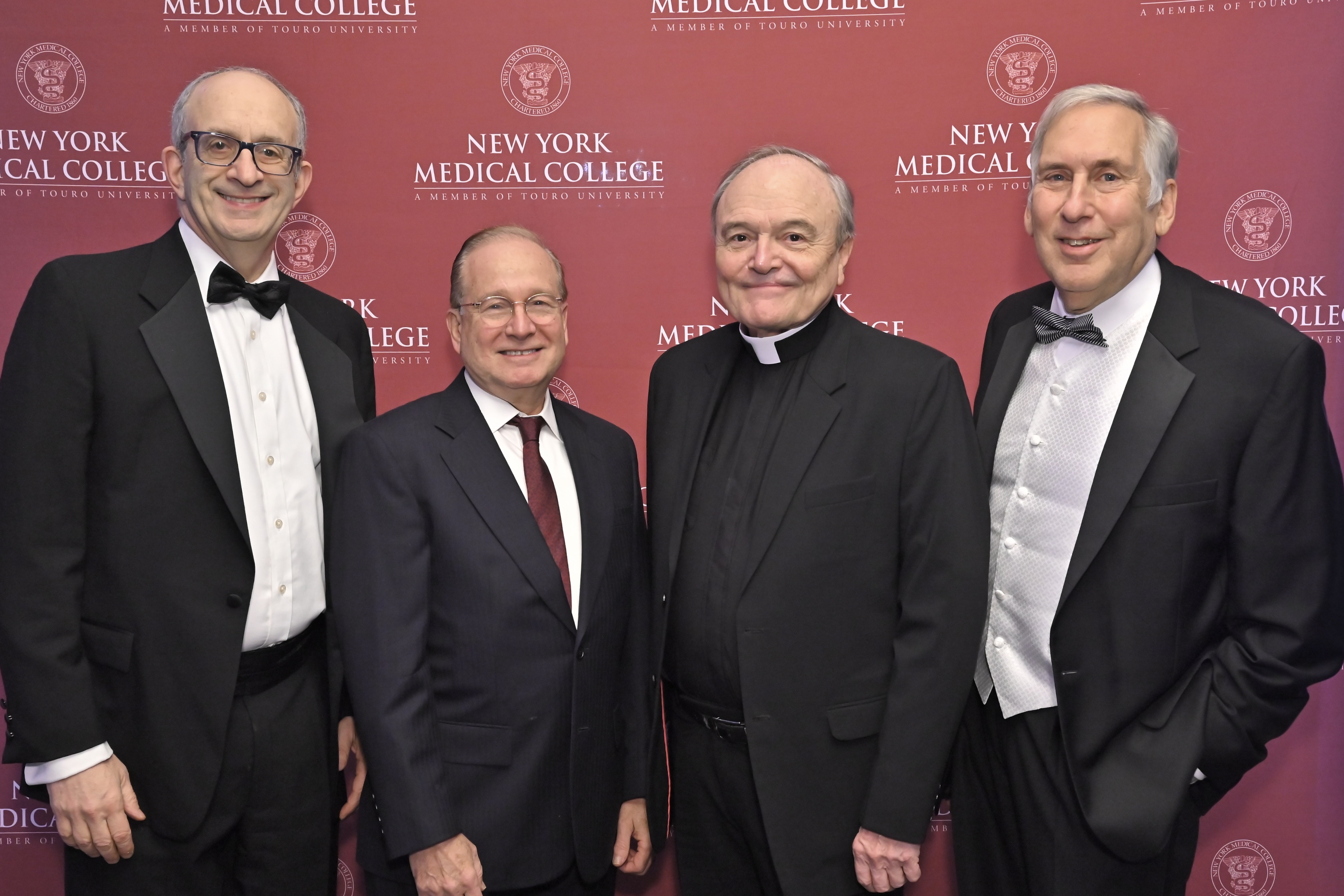 Four men in suits smiling in front of NYMC backdrop