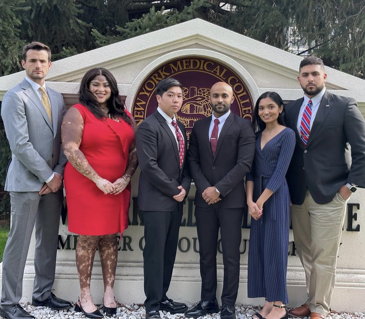 A group of diverse students smiling collectively wearing formal attire in front of New York Medical College statue
