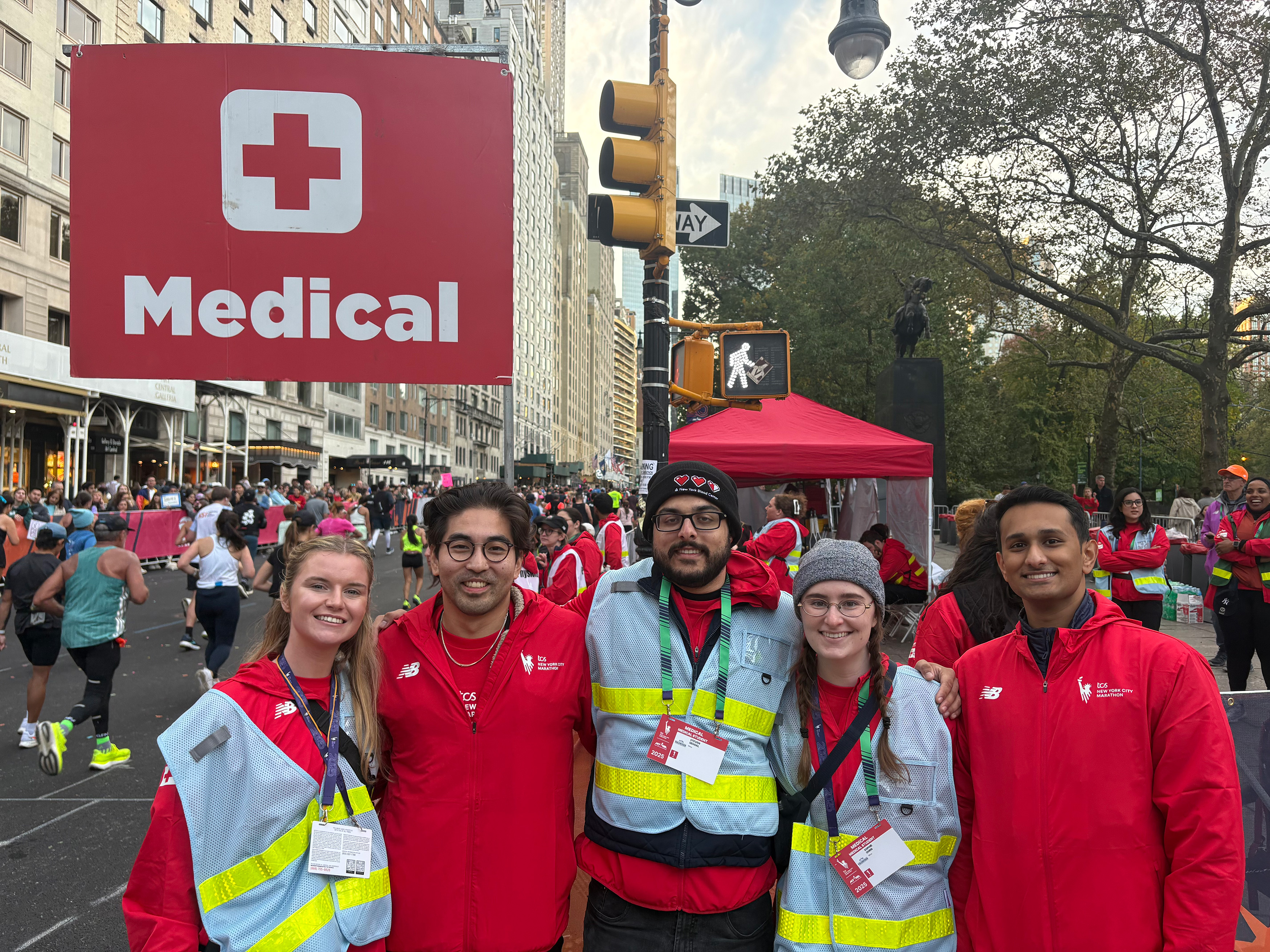 Five people wearing NYC marathon medical volunteer jackets smiling outside next to a medical sign.