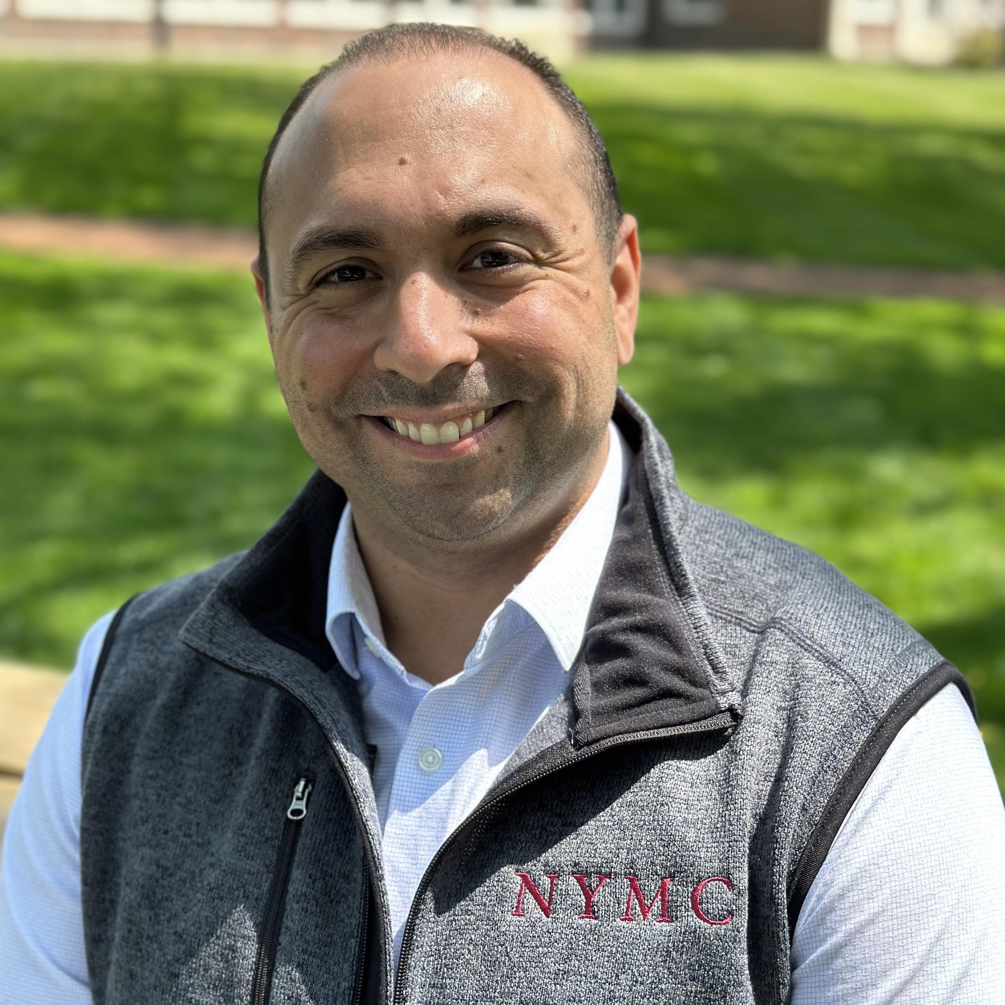 Nick Sekkas smiling outside wearing a white collar shirt and a gray vest