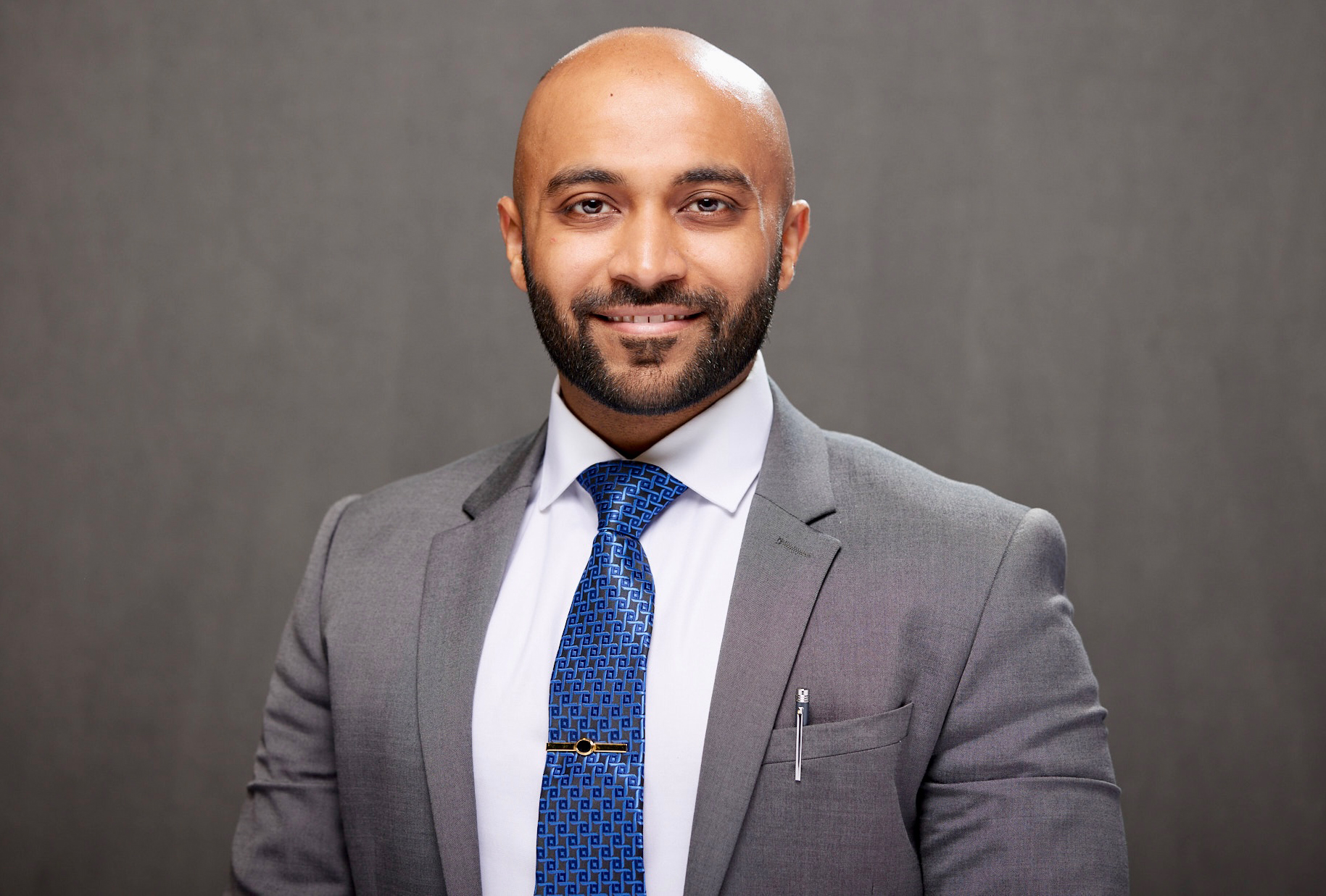 Man with beard wearing a suit smiling in front of plain background