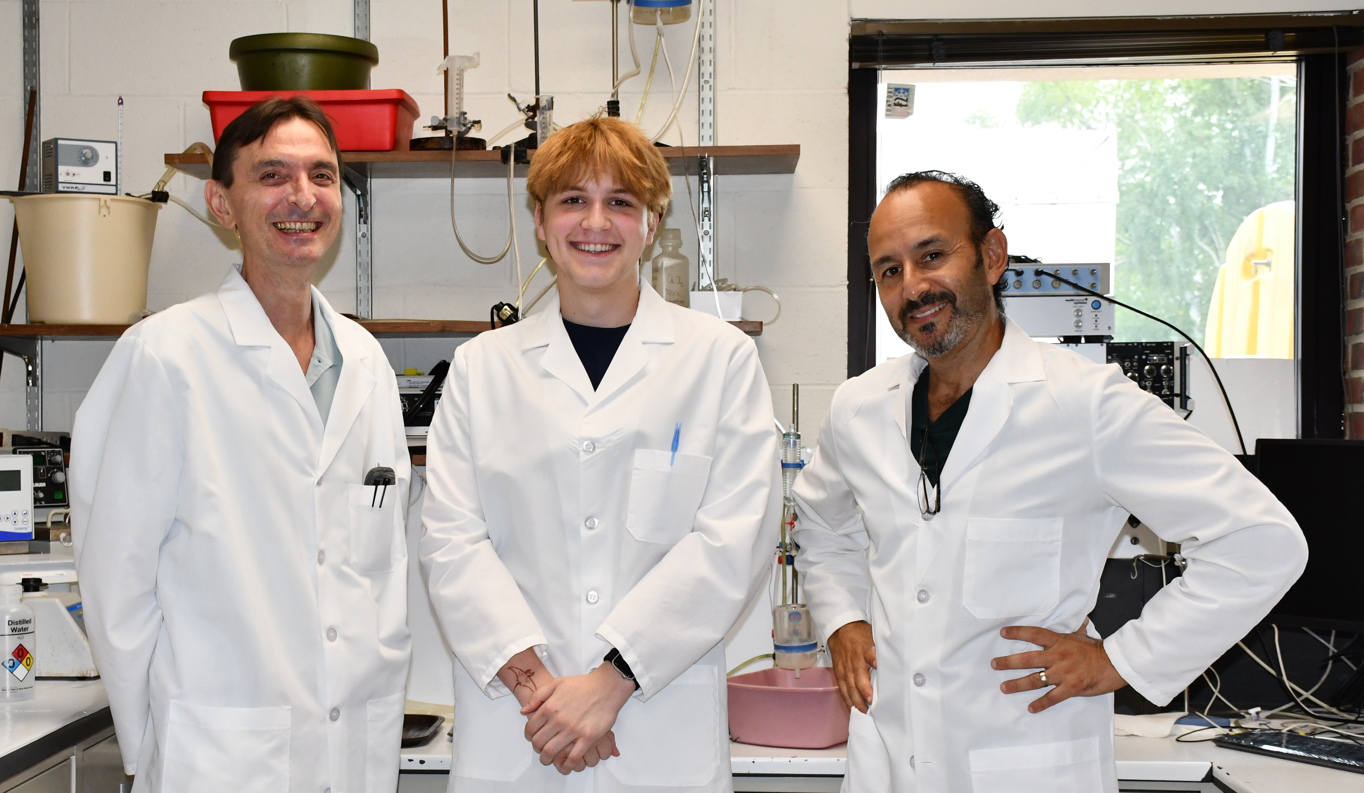 Three men wearing lab coats smiling in a lab