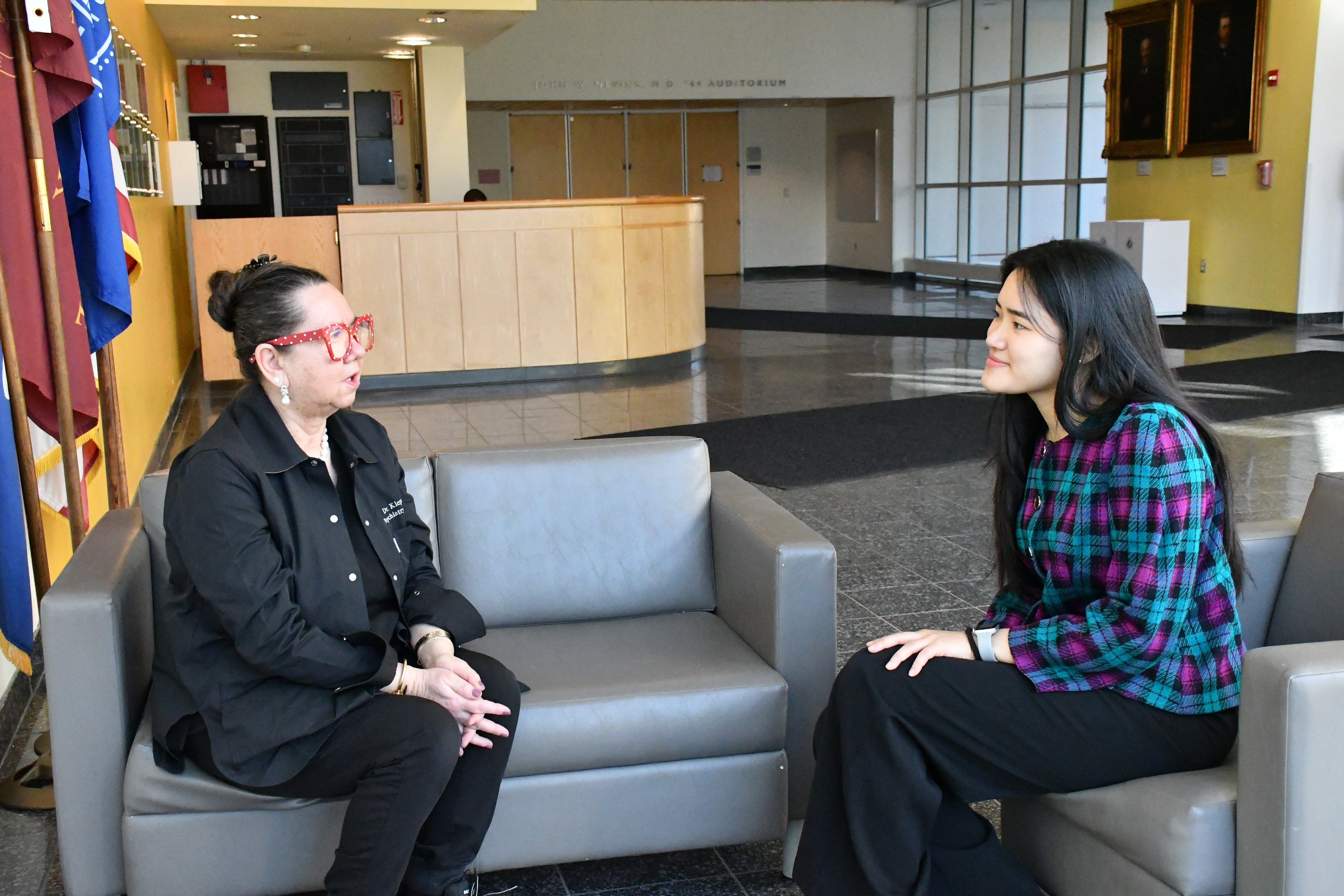 Two women in a lobby speaking on a couch